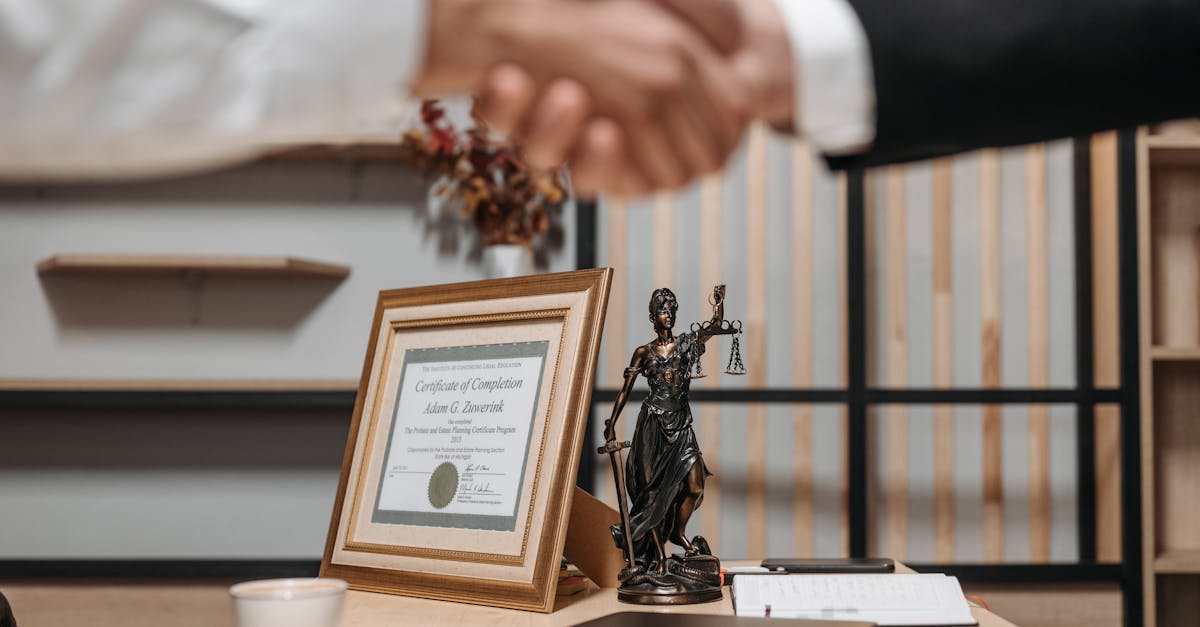 A professional handshake in an office with diploma and Lady Justice statue, symbolizing law and achievement.